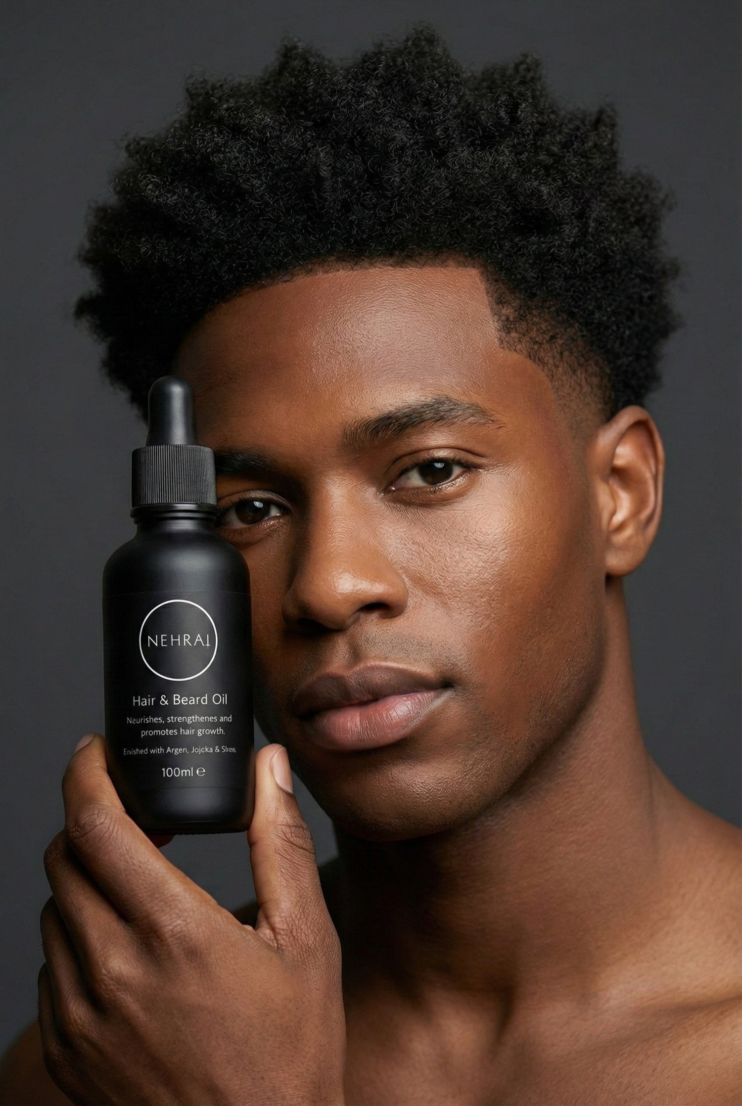 Man holding a black bottle of NEHEA hair and beard oil against a dark background